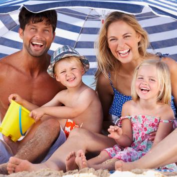 Happy family on the beach under a striped umbrella.