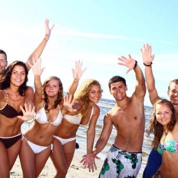 Group of friends smiling on the beach, raising their hands to the sky.