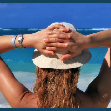 Relaxed person on beach with hat and watch.