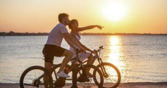Couple en vélo au coucher du soleil, près de la mer.