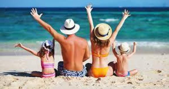Famiglia felice in spiaggia, sole splendente e mare azzurro, braccia alzate in gioia.