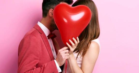 Couple s'embrassant derrière un ballon en forme de cœur.