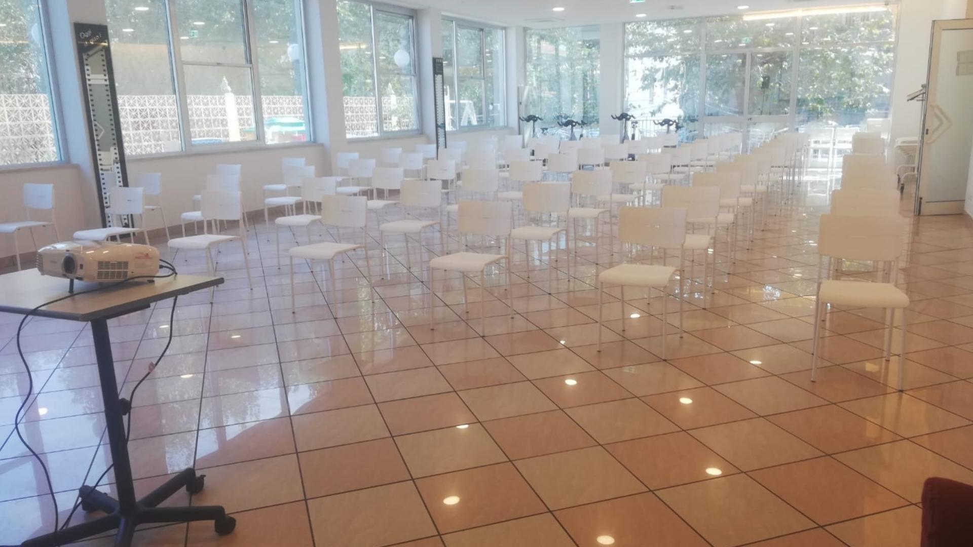 Sala luminosa con sedie bianche, proiettore pronto per una presentazione coinvolgente.