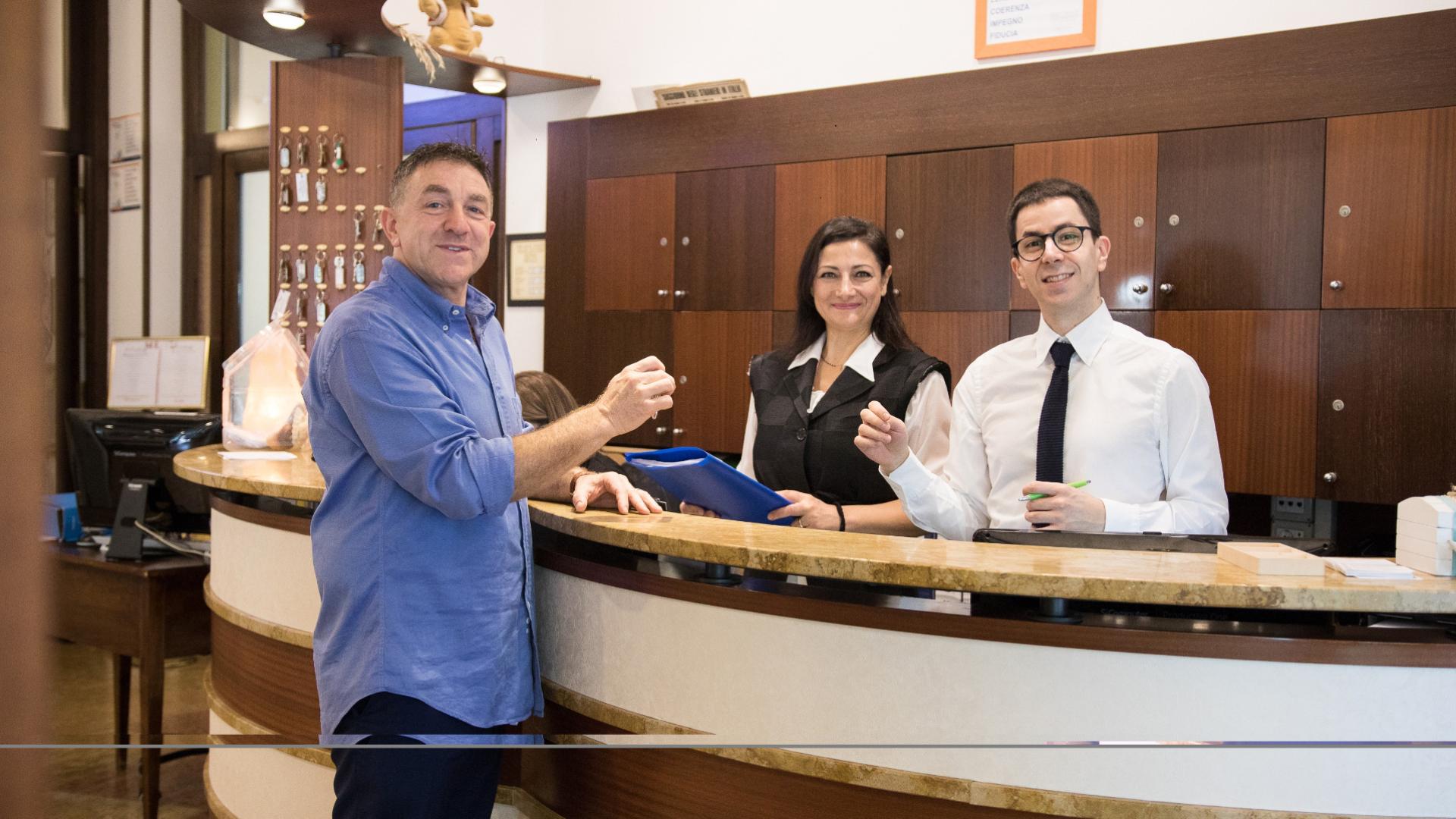 Tre persone sorridenti alla reception di un hotel, atmosfera accogliente e cordiale.