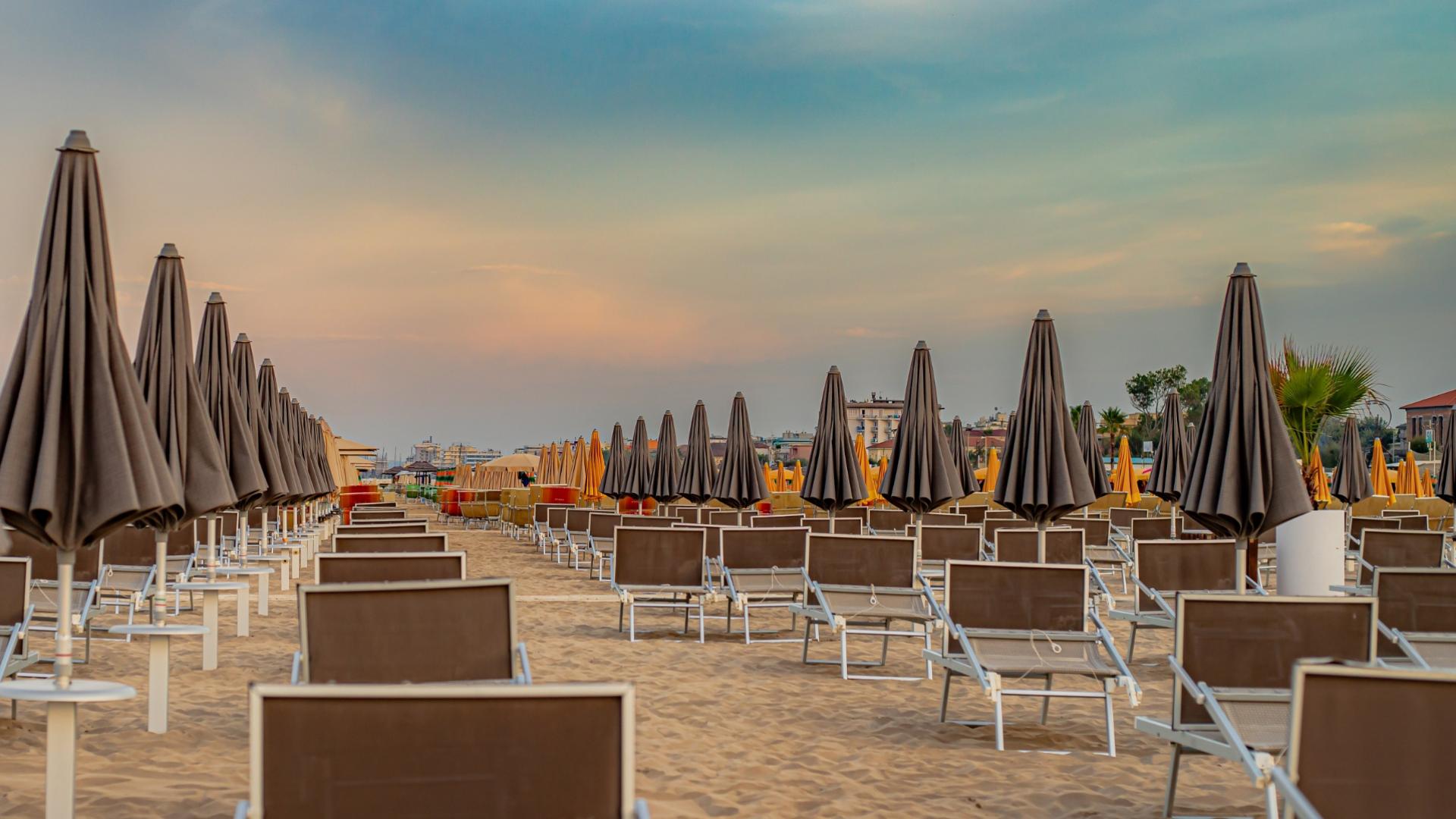 Spiaggia deserta al tramonto, ombrelloni chiusi, atmosfera tranquilla e cielo colorato.