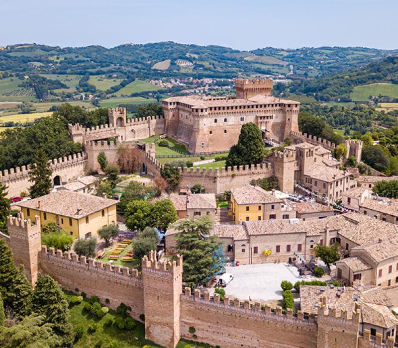Maestoso castello medievale in mattoni, circondato da un verde giardino sotto un cielo limpido.