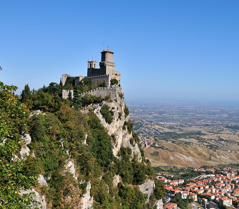 Castello medievale su una montagna, circondato da paesaggi mozzafiato e cielo sereno.