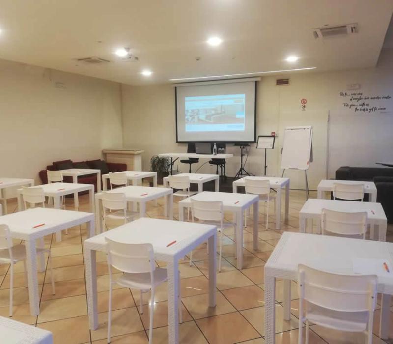 Aula luminosa, tavoli bianchi, sedie ordinate, pronte per un incontro stimolante e creativo.