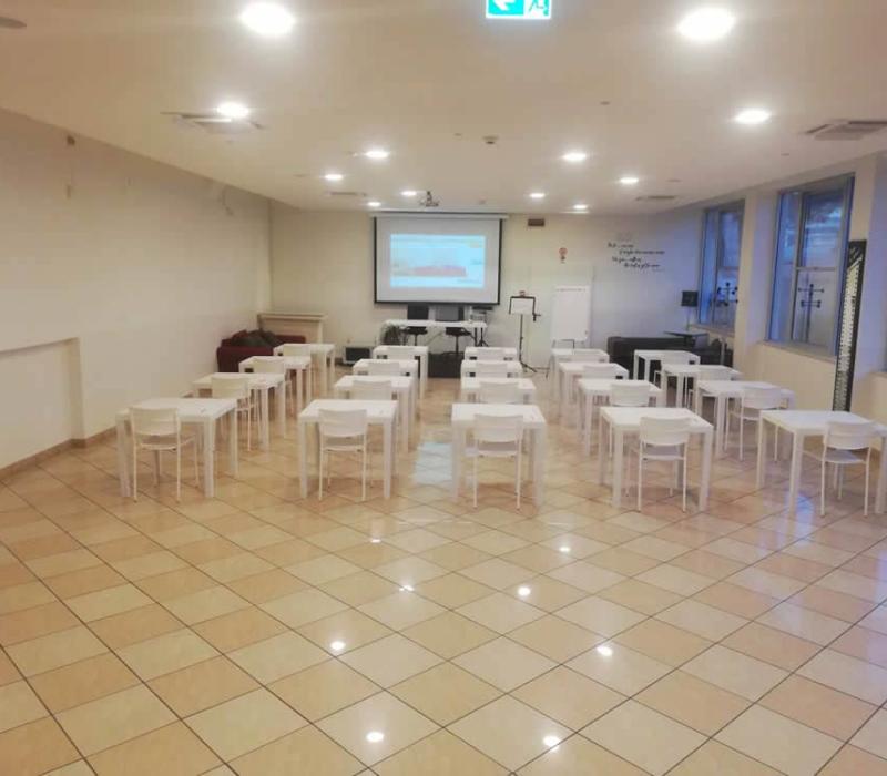 Aula luminosa e ordinata con sedie bianche, pronta per una presentazione.