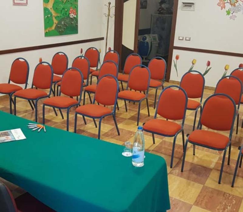 Sala conferenze accogliente, sedie arancioni, tavolo verde, decorazioni floreali, atmosfera calda e invitante.
