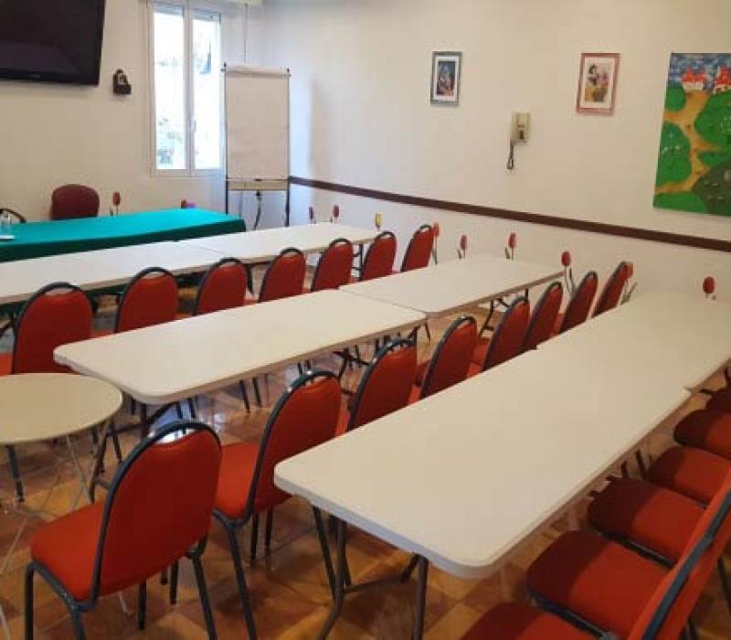 Aula luminosa con sedie rosse e tavoli bianchi, pronta per un incontro accogliente.