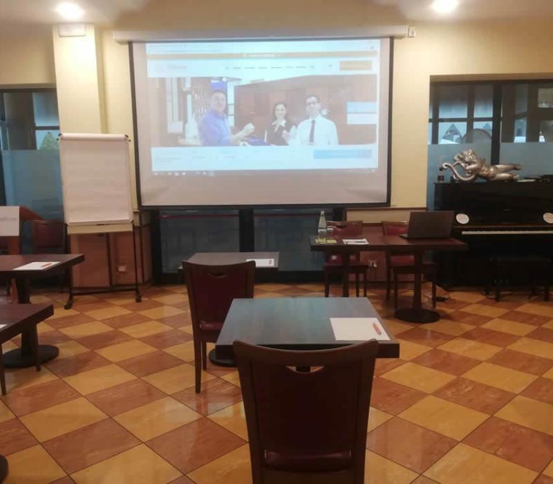 Aula accogliente con proiettore, pianoforte e tavoli pronti per un incontro formativo.